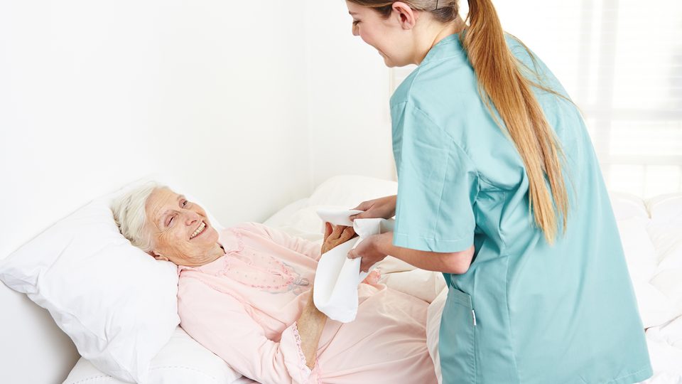 Pflegekraft versorgt eine ältere Frau im Bett