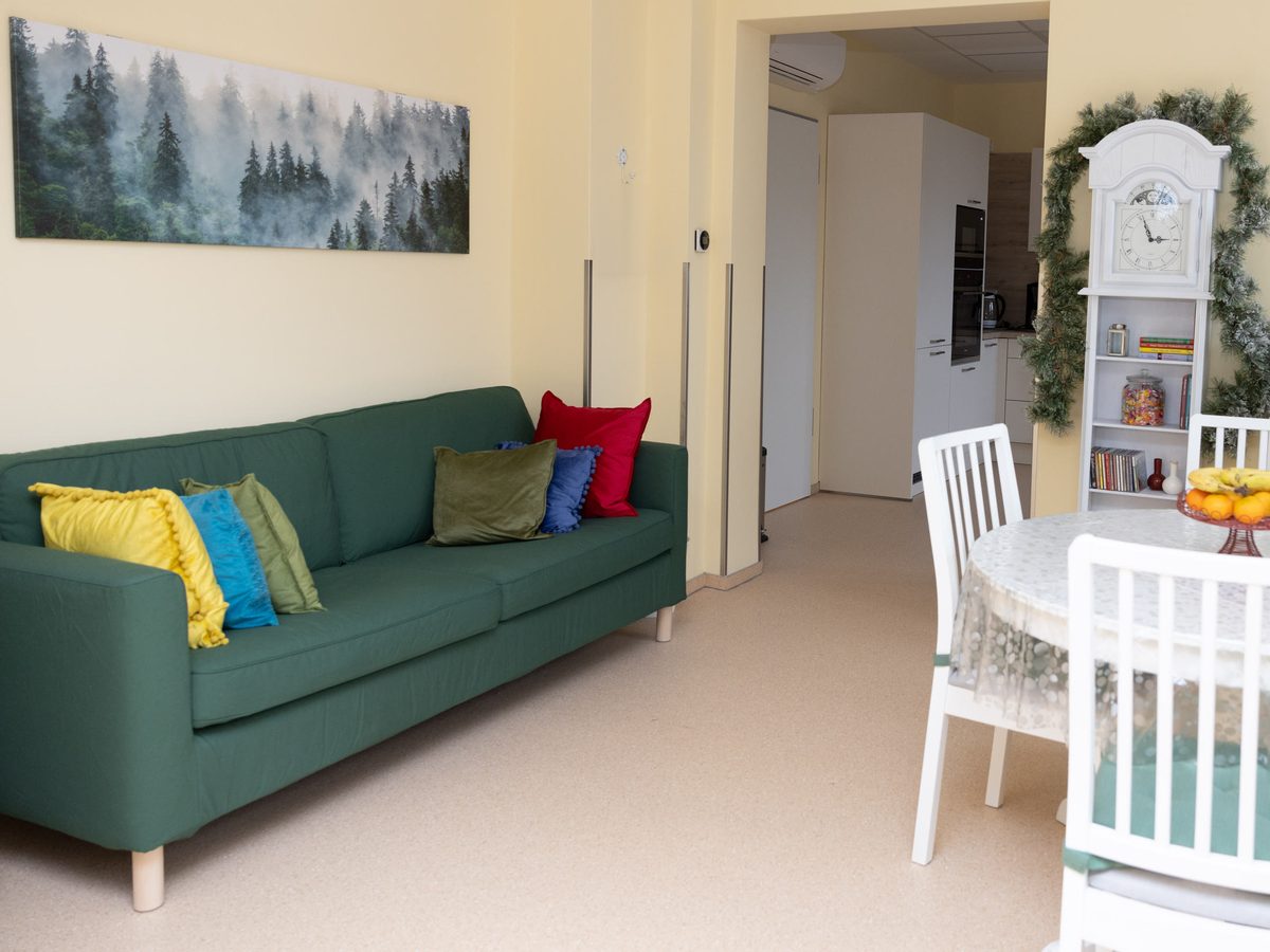 Sitzecke der Tagespflege mit grünem Sofa, bunten Kissen und rundem Tisch